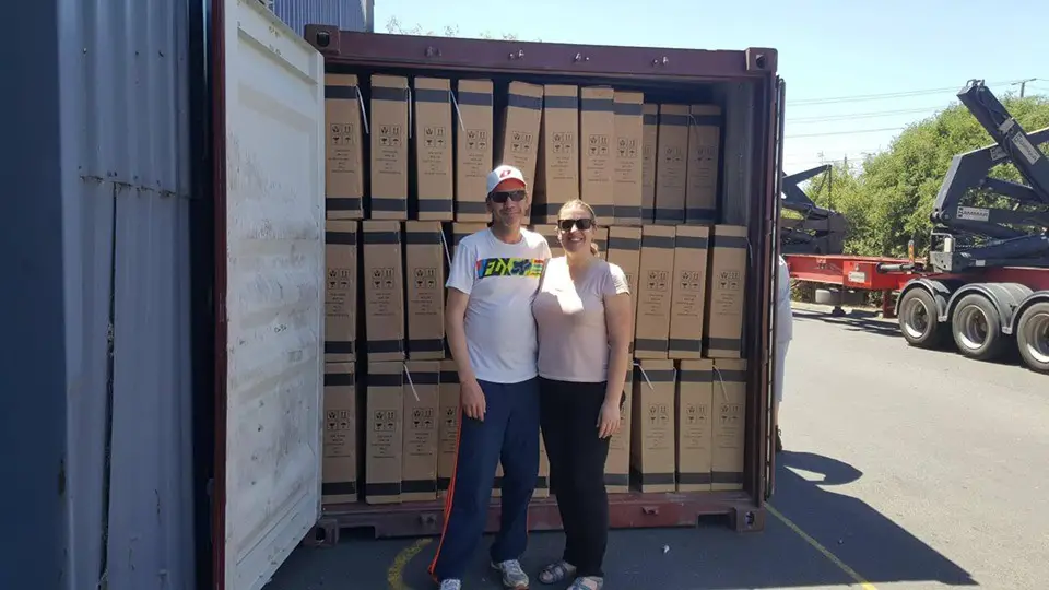 couple proudly standing in front of an opened shipping container full of boxes