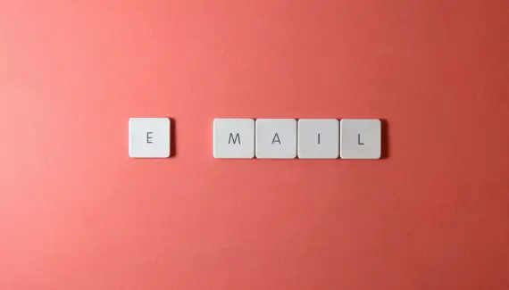 the word email on scrabble tiles, with one letter on each tile. The e is slight separate from the rest of the word. Background is clay orange.