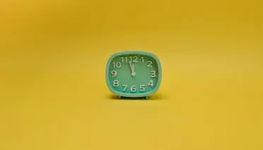 small teal anaolgue clock against a yellow background